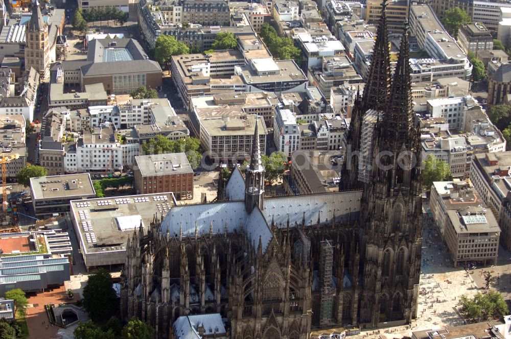 KÖLN from above - Der Kölner Dom, offizieller Name Hohe Domkirche St. Peter und Maria, ist eine römisch-katholische Kirche in Köln und die Kathedrale des Erzbistums Köln.Der Kölner Dom ist mit 157 Metern Höhe nach dem Ulmer Münster die zweithöchste Kirche in Deutschland sowie die dritthöchste der Welt. Er steht an der nördlichen ehemaligen römischen Stadtgrenze in direkter Nachbarschaft des heutigen Hauptbahnhofs, der Altstadt, Hohenzollernbrücke und Museum Ludwig und ist von einer modernen Betonkonstruktion, der sogenannten Domplatte, umgeben. Vom rund 250 Meter entfernten Rhein und vom Hauptbahnhof aus ist die Lage der Kathedrale auf dem sogenannten Domhügel, rund 17 m über dem Rhein, noch zu erahnen. Der Kölner Dom ist die weltweit drittgrößte Kathedrale im gotischen Baustil (nach der Kathedrale von Sevilla und dem Mailänder Dom). Viele Kunsthistoriker sehen in ihm eine einmalige Harmonisierung sämtlicher Bauelemente und des Schmuckwerks im Stil der mittelalterlich-gotischen Architektur verwirklicht. Der Kölner Dom wurde 1996 in die Liste des Weltkulturerbes aufgenommen. Die riesige Fläche der Westfassade mitsamt den beiden Türmen von über 7.100 Quadratmetern ist bis heute nirgendwo übertroffen worden. Von 1880 bis 1884 war er das höchste Gebäude der Welt. Er ist zudem die populärste Sehenswürdigkeit Deutschlands: 2001 wurden fünf Millionen, 2004 sechs Millionen Besucher aus aller Welt gezählt.