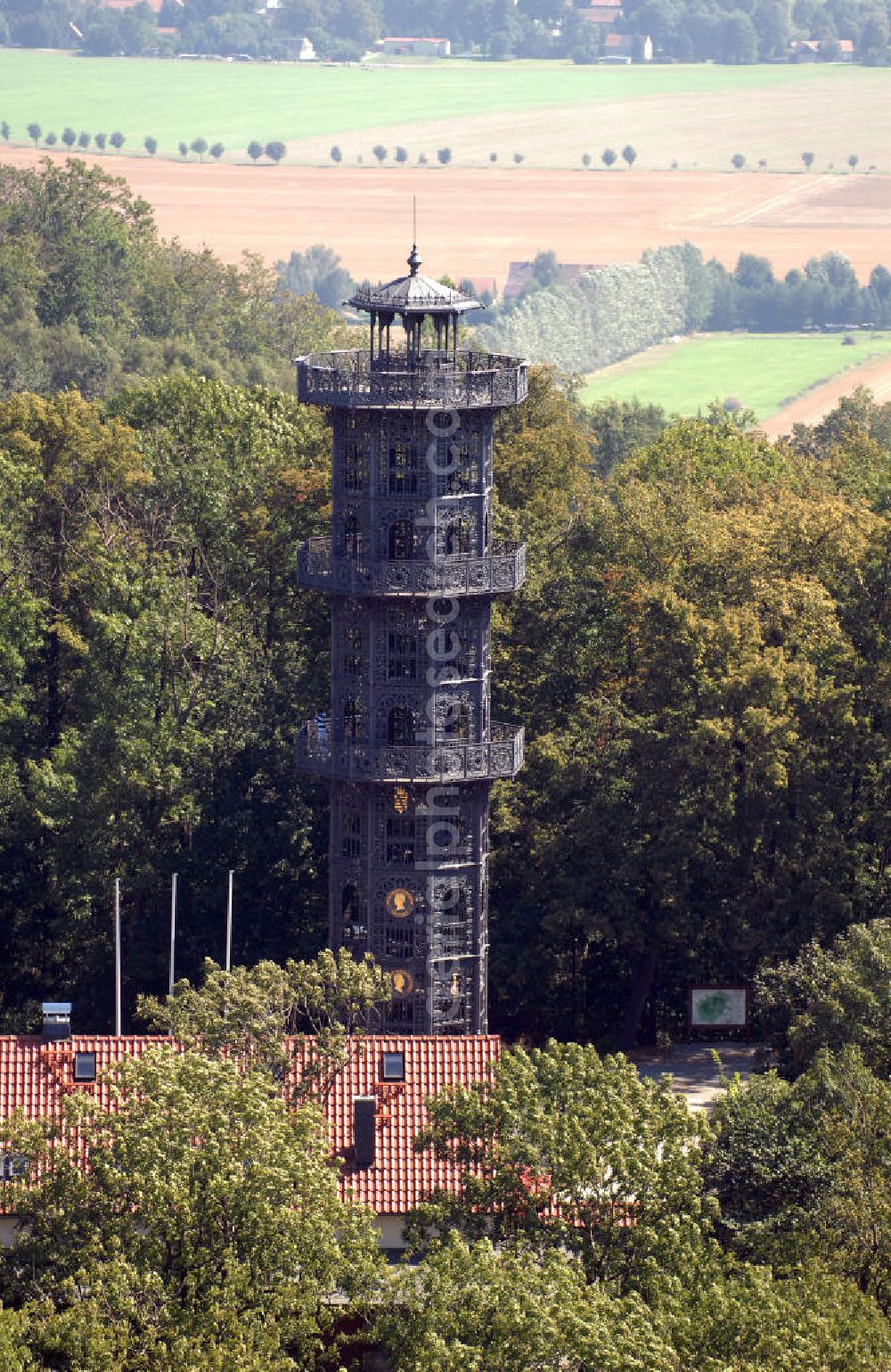 Aerial image Löbau - Der König-Friedrich-August-Turm auf dem Löbauer Berg im sächsischen Löbau ist der einzige noch erhaltene gusseiserne Aussichtsturm in Europa und wahrscheinlich der älteste gusseiserne Turm überhaupt. Er wurde 1854 aus Gusseisen errichtet, weist eine Höhe von 28 Metern und einen Durchmesser von vier Metern auf, hat eine achteckige Form und enthält drei außenliegende Galerien in 12, 18 und 24 Meter Höhe. Die innenliegende Wendeltreppe hat 120 Stufen. Auf der Aussichtsplattform befindet man sich insgesamt in einer Höhe von 28 Metern. Vom Turm aus kann man bis zum Zittauer Gebirge und über weite Teile der Landschaft der Oberlausitz blicken. Der nach dem sächsischen König Friedrich August II. benannte Turm steht mittlerweile als technisches Denkmal unter Denkmalschutz und ist ein beliebtes, weithin bekanntes Ausflugsziel.