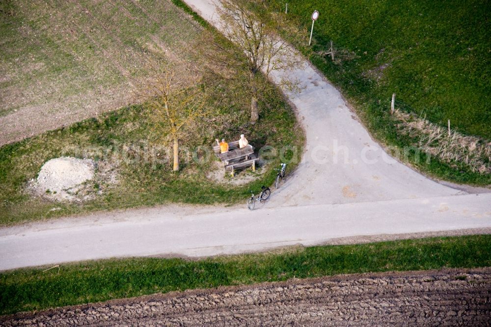 Aerial image Raisting - Older married couple sit on a bank on the edge of a crossroads and waves in the district of Stillern in Raisting in the federal state Bavaria