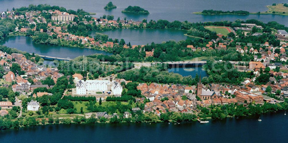 PLÖN from the bird's eye view: 22.06.2004 PLÖN Plön besitzt seit 1236 Stadtrechte; ist seit dem 17. Jh. Residenz der Herzöge von Schleswig-Holstein-Sonderburg-Plön.Plön ist die Kreisstadt des Kreises Plön in Schleswig-Holstein und hat etwa 13.000 Einwohner. Sie liegt direkt am größten Binnensee Schleswig-Holsteins, dem Großen Plöner See. Wahrzeichen der Stadt ist das Schloss, das im 17. Jahrhundert erbaut wurde. Plön besitzt ein Gymnasium mit 300-jähriger Geschichte, ist Standort einer Marineunteroffizierschule und Sitz des Max-Planck-Instituts für Evolutionsbiologie. Die in die hügelige Seenlandschaft der Holsteinischen Schweiz eingebettete Stadt hat auch touristische Bedeutung. Das Plöner Schloss wurde 2001 unter der Landesregierung von Heide Simonis geschlossen und an den Optikerkonzern Fielmann verkauft. Dieser hat dort nach umfangreichen Restaurierungsarbeiten im Oktober 2006 eine Akademie für das Optikerhandwerk eröffnet. Es handelt sich um ein gemeinnütziges Schulungszentrum für die gesamte Augenoptik. Dies bedeutet für die Stadt Plön eine Stärkung der Wirtschaftskraft und eine herausragende Werbung, auch über die Landesgrenzen hinaus. Zum Schloss gehört das weitläufige Schlossgebiet, das zu den schönsten Schlossanlagen Schleswig-Holsteins gehört. Aufwendig restaurierte historische Gebäude (z.B. Prinzenhaus, Alte Schwimmhalle, Uhrenhaus), schattige Alleen und alter Baumbestand laden zum Erkunden und Flanieren ein.