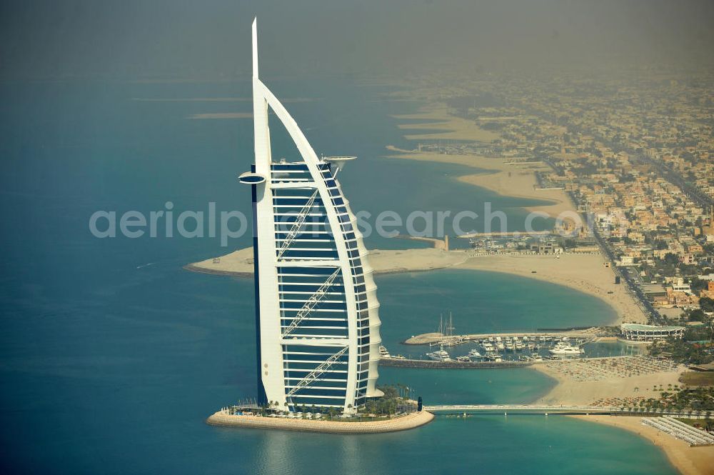 DUBAI / DUBAYY from the bird's eye view: Blick auf das Luxus- Hotel Burj al Arab am Persischen Golf in Dubai. Der architektonisch einprägsame Bau der Jumeirah Group ist eines der luxuriösesten und teuersten Hotels der Welt. Mit einer Höhe von 321 Metern ist es nach dem Rose Tower das höchste reine Hotelgebäude der Welt und ein Wahrzeichen der emiratischen Stadt Dubai. Der Entwurf stammt von Tom Wright / Atkins Middle East. Ausdrücklicher Wunsch der Bauherren war es, eine Architekturikone zu schaffen, die ein Identifikationsmerkmal für Dubai wird. Der Entwurf hat die Form des Segels einer modernen Yacht und soll die Vergangenheit als Seehandelszentrum sowie die Zukunftsorientierung Dubais symbolisieren. Luxury hotel Burj al Arab on Persian Gulf in Dubai.