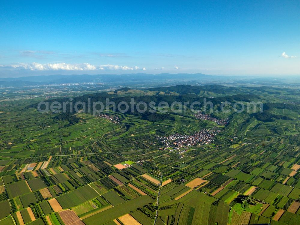 Vogtsburg im Kaiserstuhl from the bird's eye view: Low mountain range Kaiserstuhl and Totenkopf (Skull) mountain in Vogtsburg in the state of Baden-Wuerttemberg. The landscape of the mountain range in this region is characterised by terrace-like vineyards and mountain tops covered in mixed forest around which villages and fields are grouped. The foreground shows the village of Kiechlinsbergen, Totenkopf mountain - the highest mountain of the mountain range - is located in the background