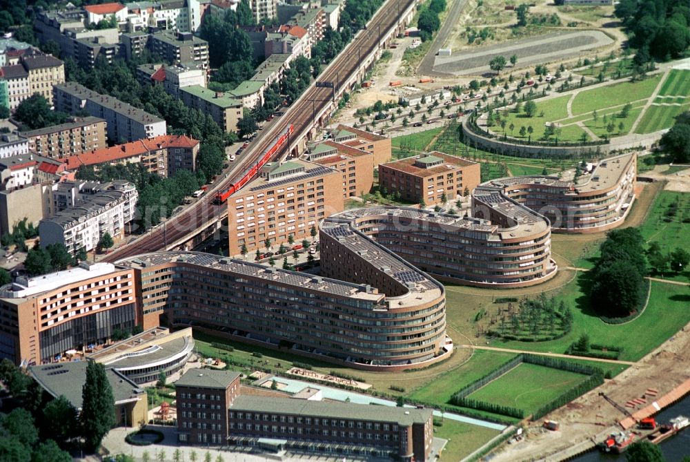 Aerial photograph Berlin-Moabit - Views are called with the distinctive residential buildings, the Bundestagsnake around the Moabiter Werder in Berlin-Mitte. Architect Georg Bumiller designed the building with the wavy outline along the S-Bahn line. The focus is housed in a former elementary school building logistics. In the background, the chancellor park with paths oval scale