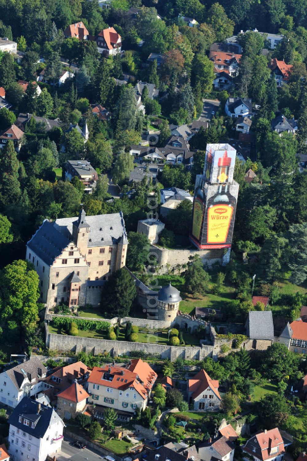 Kronberg im Taunus from the bird's eye view: Blick auf eine Maggiflasche als Großwerbeplakat auf der Einrüstung der Burg Kronberg. Zum 125-jährigen Jubiläum der Maggi-Würzsoße wurde der im Volksmund als Maggi-Flasche bezeichnete Turm des Kronberger Wahrzeichens für drei Monate als Werbeträger genutzt. Die Werbeeinnahmen der NESTLE Gruppe fließen unmittelbar in die Burgsanierung. View a bottle of Maggi at Burg Kronberg.