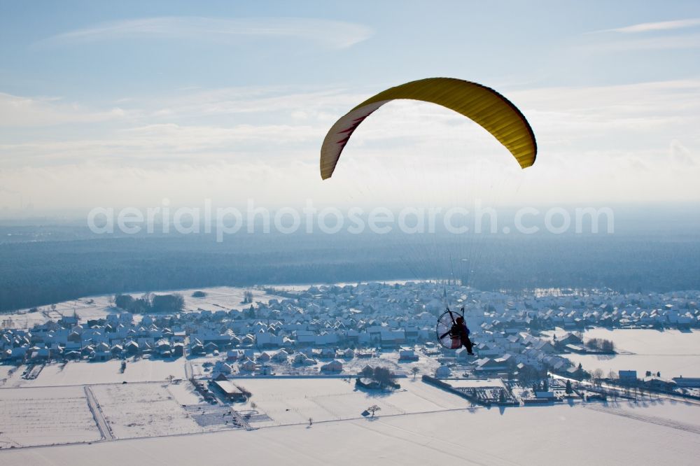 Hatzenbühl from above - Powered paraglider flying over winterly snow-covered village in Hatzenbuehl in the state Rhineland-Palatinate