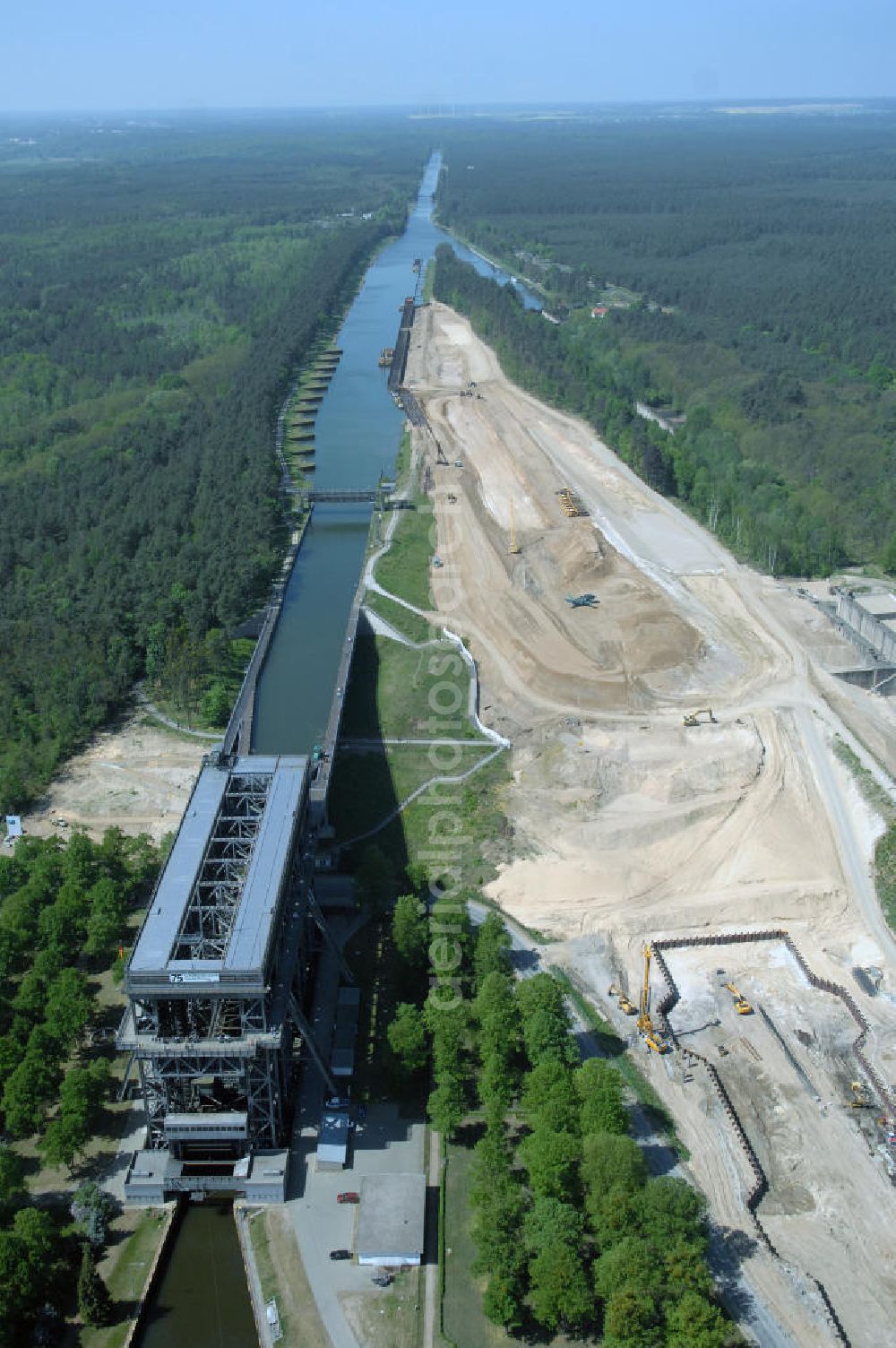 Aerial image NIEDERFINOW - Das Wasserstraßen-Neubauamt Berlin den Bauauftrag für den Neubau des Schiffshebewerkes Niederfinow Nord vergeben. Der Zuschlag wurde auf das Angebot der Bietergemeinschaft Neues Schiffshebewerk Niederfinow unter Federführung der Bilfinger Berger AG erteilt. Der Bietergemeinschaft gehören weiter: die DSD Brückenbau GmbH, die Johann Bunte Bauunternehmung GmbH & Co. KG und die Siemag GmbH an. Die geplante Bauzeit für das neue Schiffshebewerk beträgt fünf Jahre, die Baukosten für die Gesamtanlage liegen bei rd. 285 Mio. Euro und werden durch den Bund finanziert. Seit Mitte Februar 2009 wird die Baugrubenumschließung für das neue Schiffshebewerk hergestellt. Es werden 217 Träger und 214 Zwischenbohlen in den Baugrund eingebracht. Die Träger haben eine Länge von ca. 22m und wiegen einzeln etwa 5,7 Tonnen. Die Rüttelarbeiten für die Baugrube werden voraussichtlich bis Ende April andauern.Mit einem Investitionsvolumen von rd. 285. Mio € entsteht in Niederfinow bis zum Jahr 2014 ein neues Schiffshebewerk der europäischen Wasserstraßenklasse V. Der Neubau ist dringend erforderlich, weil das alte Schiffshebewerk aus dem Jahr 1934 bald das Ende seiner Lebensdauer erreicht hat. Um die Funktion der Havel-Oder-Wasserstraße aufrechtzuerhalten, muss es daher planmäßig durch einen Neubau ersetzt werden.