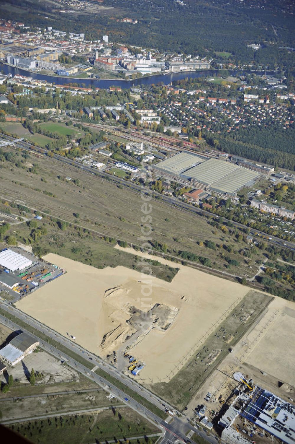 Aerial photograph Berlin - Blick auf eine Planfläche im Gewerbegebiet Flugplatz Johannisthal am Groß-Berliner Damm. Das Gelände dient heute als Baufläche für Einfamilienhäuser und als Gewerbegebiet. Des weiteren befindet sich heute auf dem Gelände unter an derem der Aerodynamische Park als Teil des Campus der Humboldt-Universität zu Berlin. Der Name des Platzes weist auf den besonderen Charakter und die historische wie architektonische Bedeutung durch die prägnanten und dominierenden Baudenkmale der ehemaligen Deutschen Versuchsanstalt für Luftfahrt e.V. hin. Das mittlerweile entstandene grüne Biotop auf der Fläche der ehemaligen Start- und Landebahn ist in eine Parklandschaft integriert worden, dem Europapark, der nach einem Wettbewerb seit den späten 1990er Jahren hier entsteht. View onto the construction site at the industrial area at the former airport Johannisthal. Today the area serves as ab building area and as an industrial area.