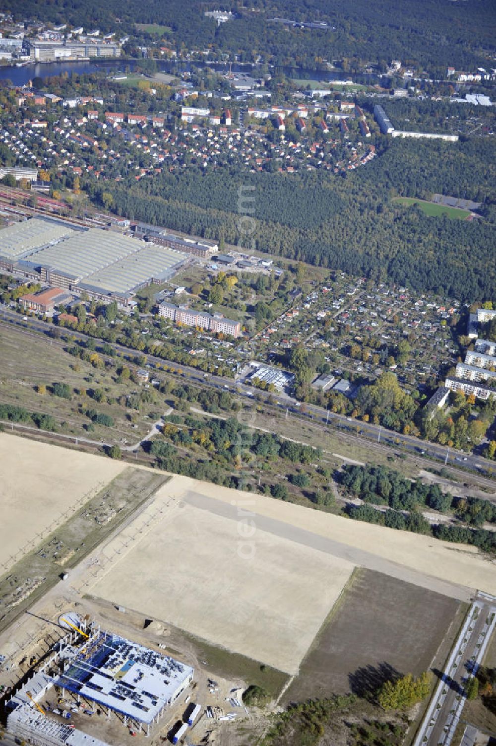 Berlin from the bird's eye view: Blick auf eine Planfläche im Gewerbegebiet Flugplatz Johannisthal am Groß-Berliner Damm. Das Gelände dient heute als Baufläche für Einfamilienhäuser und als Gewerbegebiet. Des weiteren befindet sich heute auf dem Gelände unter an derem der Aerodynamische Park als Teil des Campus der Humboldt-Universität zu Berlin. Der Name des Platzes weist auf den besonderen Charakter und die historische wie architektonische Bedeutung durch die prägnanten und dominierenden Baudenkmale der ehemaligen Deutschen Versuchsanstalt für Luftfahrt e.V. hin. Das mittlerweile entstandene grüne Biotop auf der Fläche der ehemaligen Start- und Landebahn ist in eine Parklandschaft integriert worden, dem Europapark, der nach einem Wettbewerb seit den späten 1990er Jahren hier entsteht. View onto the construction site at the industrial area at the former airport Johannisthal. Today the area serves as ab building area and as an industrial area.