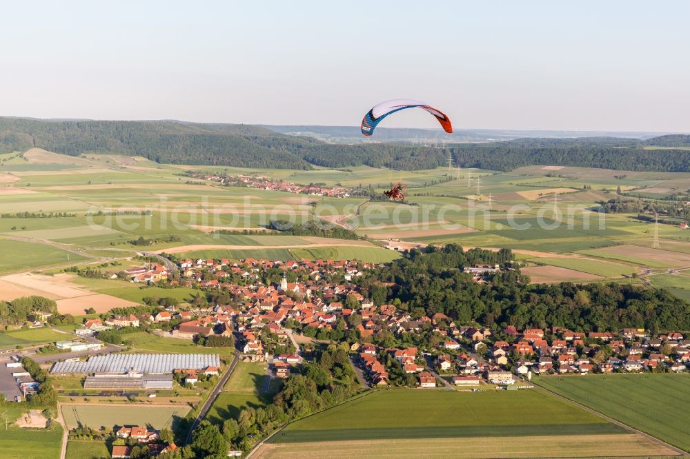 Rüdenhausen from above - Paradlider over a Village on the edge of agricultural fields and farmland in Ruedenhausen in the state Bavaria, Germany