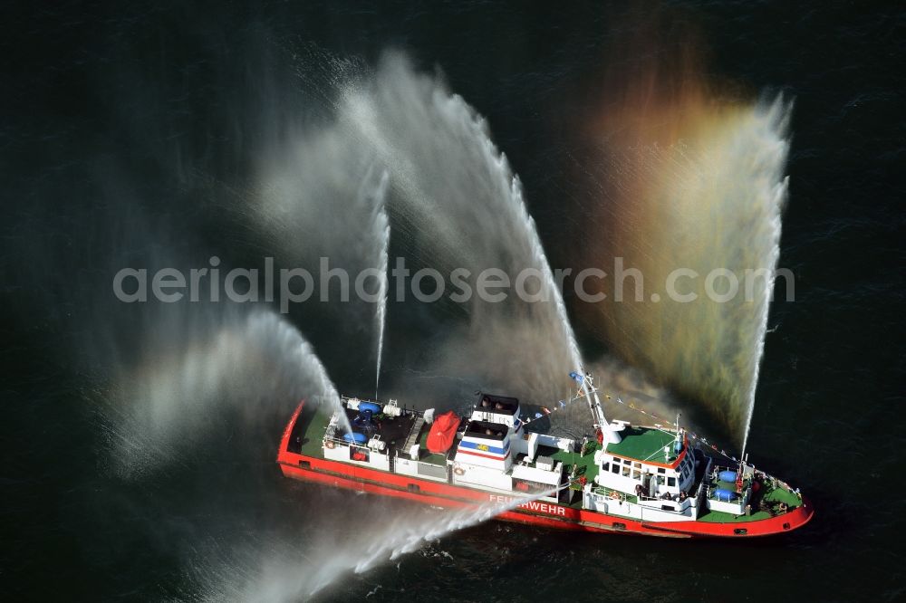 Rostock from above - Colorful colored rainbow water fountains of traditional fire extinguishing ship welcoming the sailing ships of the Hanse Sail maritime leak on the Baltic Sea in Rostock in Mecklenburg - Western Pomerania