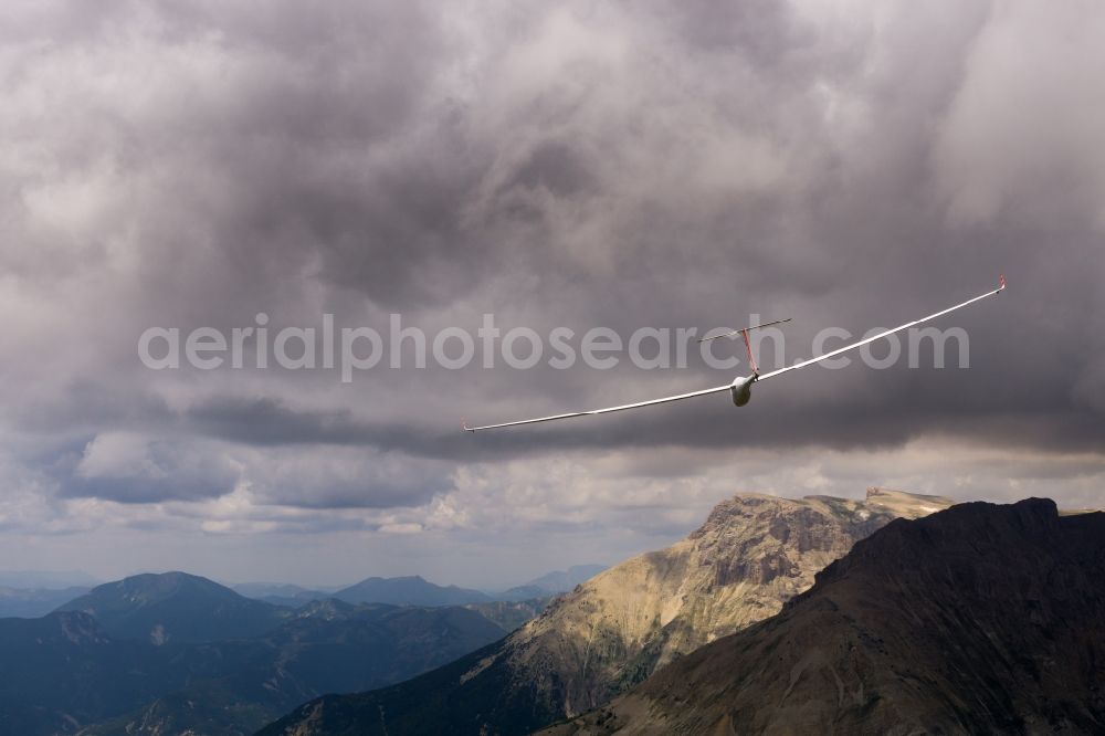 La Roche-des-Arnauds from the bird's eye view: Glider ASH 26 flying below dark clouds and rugged rocks in La Roche-des-Arnauds in Provence-Alpes-Cote d'Azur, France