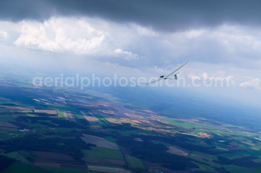 Seedorf from the bird's eye view: Glider and sport aircraft Duo Discus D-KBFV flying under dark clouds over the airspace in Seedorf in the state Lower Saxony, Germany