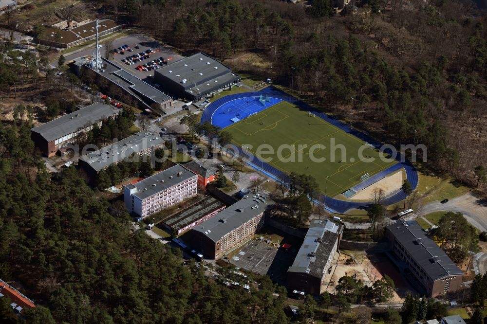 Kleinmachnow from the bird's eye view: Sports facilities of the Berlin Brandenburg International School and residential buildings in Kleinmachnow in the state of Brandenburg. The BBIS includes a football pitch and athletics facilities in a distinct blue colour. Residential buildings and estates as well as a primary school are surrounded by trees and woods