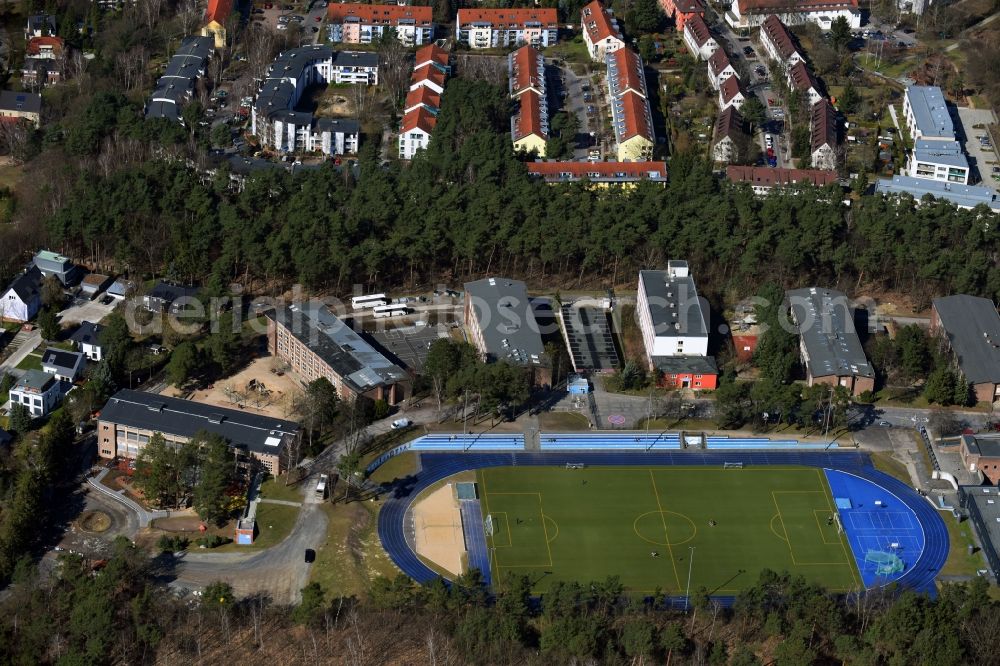 Kleinmachnow from the bird's eye view: Sports facilities of the Berlin Brandenburg International School and residential buildings in Kleinmachnow in the state of Brandenburg. The BBIS includes a football pitch and athletics facilities in a distinct blue colour. Residential buildings and estates as well as a primary school are surrounded by trees and woods