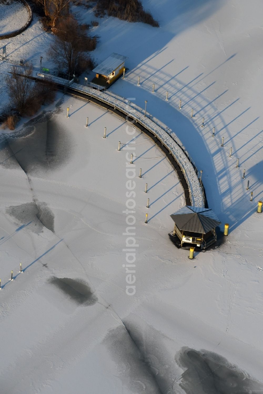 Beetzsee from the bird's eye view: Recreational marine jetties and moorings on the shore area of the wintry snow and ice covered Beetzsee in Brandenburg