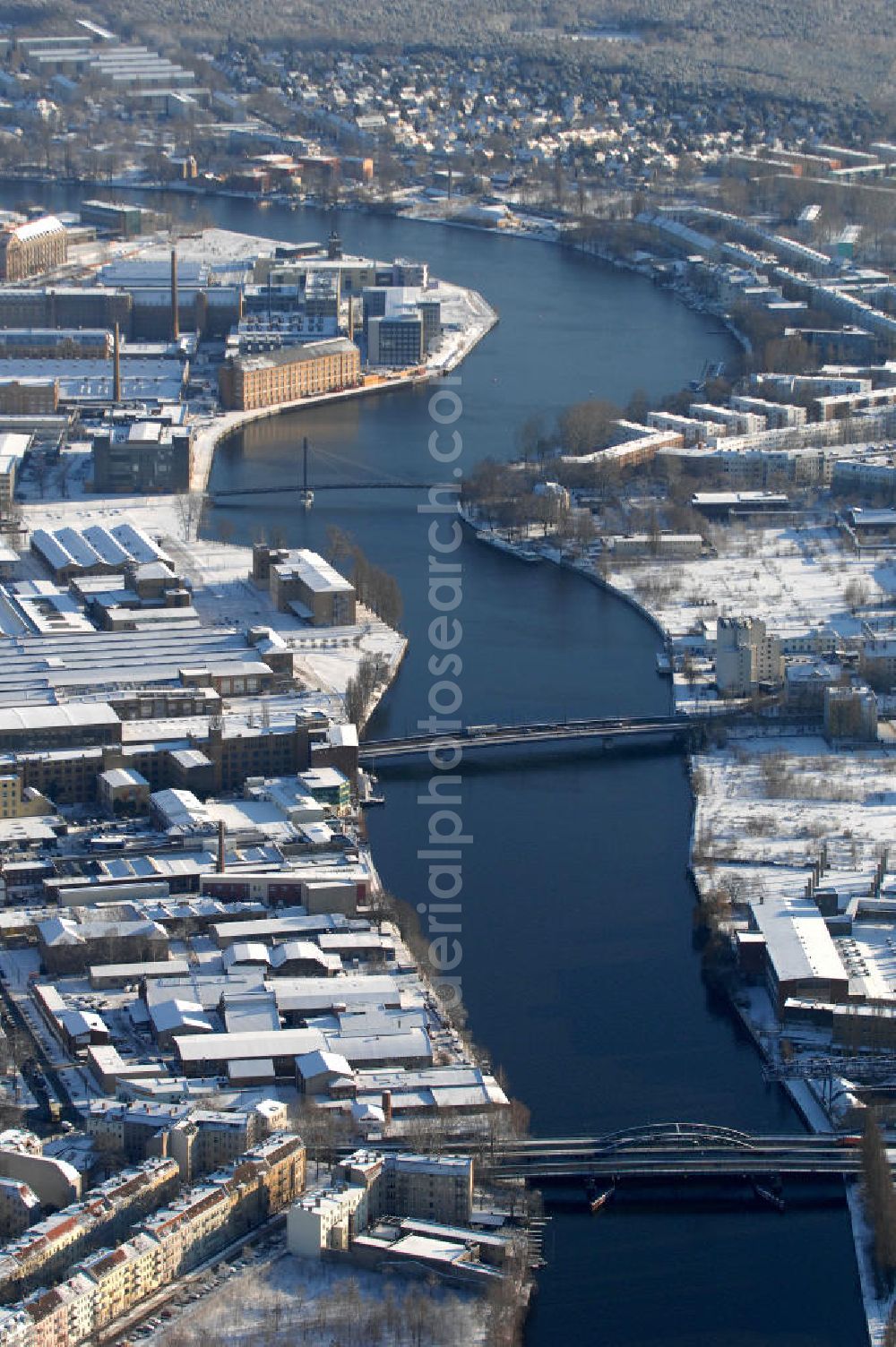 Berlin from the bird's eye view: Blick auf die Spree mit den winterlich Schnee bedeckten Stadtteilen Oberschöneweide (l) und Niederschöneweide (r). Die beiden Stadtteile sind über die Straßenbrücke Neue Treskowbrücke (v) und über die Fussgängerbrücke Kaisersteg (h) miteinan der verbunden.