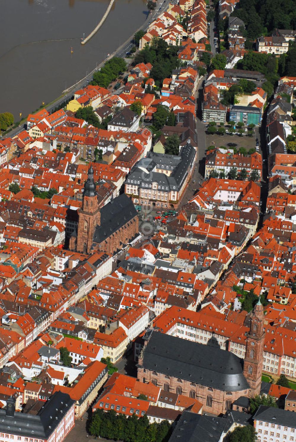 Heidelberg from above - Stadtansicht mit Blick auf zwei Kirchen Heidelbergs. Heidelberg ist eine Großstadt am Neckar im Südwesten Deutschlands. Mit über 140.000 Einwohnern ist Heidelberg die fünftgrößte Stadt Baden-Württembergs. Sie ist kreisfreie Stadt und zugleich Sitz des umliegenden Rhein-Neckar-Kreises. Die Heiliggeistkirche (mitte) ist die bekannteste Kirche von Heidelberg. Sie steht am Marktplatz mitten im alten Zentrum von Heidelberg, nur unweit vom Heidelberger Schloss entfernt und beherrscht mit ihrer weit über die Dächer ragenden Silhouette das ganze Stadtbild. Die Heiliggeistkirche wurde 1239 zum ersten Mal erwähnt. 1398 wurde der Grundstein für ihre heutige, spätgotische Form gelegt, welche die damalige spätromanische Basilika gleichen Namens ersetzte, die selbst auch nicht der ursprüngliche Bau war. Kontakt: Heiliggeistkirche, Heiliggeiststr. 17, 69117 Heidelberg, Tel.: 06221 21117, http://heiliggeist.ekihd.de. Unweit der Heiliggeistkirche befindet sich auch die Jesuitenkirche (unten). Sie ist das Wahrzeichen der Gegenreformation in Heidelberg und bildete einst den Mittelpunkt des ehemaligen Jesuitenviertels. Sie ist heute die Hauptkirche der römisch-katholischen Heilig-Geist-Gemeinde. Der Bau der Jesuitenkirche wurde in den Jahren 1712 bis 1723 unter der Leitung von Johann Adam Breuning begonnen. Die Fertigstellung erfolgte jedoch erst 1759 unter dem Architekten des kurpfälzischen Hofes, Franz Wilhelm Rabaliatti. 1793 - 1797 wurde die Jesuitenkirche als Lazarett für Verwundete des ersten Koalitionskrieges genutzt. Kontakt: Jesuitenkirche Heidelberg, Merianstr. 2, 69117 Heidelberg, Tel.: 06221 / 9008-0,