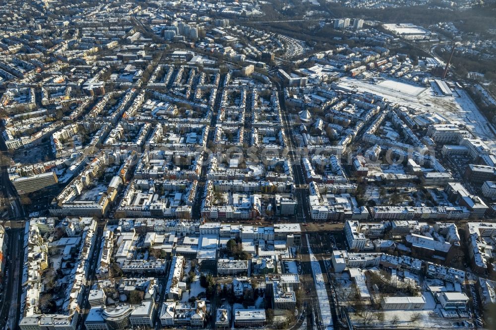 Aerial photograph Essen - Cityscape of the winterly and snow-covered Ruettenscheid part of Essen in the state of North Rhine-Westphalia. The district is located in the South of downtown Essen and is home to several symmetrical, almost rectangular, apartment blocks. It is also home to several public institutions and buildings such as the police headquarters, court buildings, a prison and a clinic for forensic psychiatry