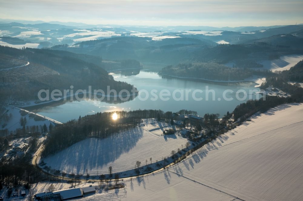 Aerial image Meschede - Winterly snowy impoundment and shore areas at the lake Hennesee aswell as surrounding fields and forestland in Meschede in the state North Rhine-Westphalia