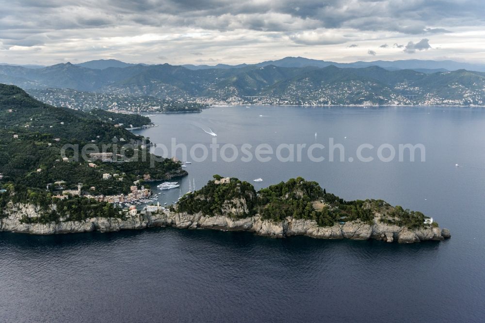 Portofino from above - Cliff coast in Mediterranean Sea with view on the harbor bay in Portofino in Liguria in Italy. The museum Castello Brown stands in the right corner. The mountains of the Alps are visible in the background