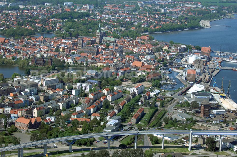 Stralsund from above - Mit dem Begriff Strelasundquerung werden die beiden Brückenverbindungen der Insel Rügen über den Strelasund zum vorpommerschen Festland bei Stralsund, die Rügenbrücke und der Rügendamm, sowie die regelmäßig betriebenen Fährverbindungen zwischen Stralsund und Altefähr sowie Stahlbrode und Glewitz bezeichnet. Der Rügendamm ist die erste feste Strelasundquerung, über den sowohl die alte Bundesstraße 96, als auch eine eingleisige Eisenbahnstrecke sowie ein kombinierter Fuß- und Radweg führen. Sie wurde 1936/1937 fertiggestellt. Rügenbrücke ist der Name der im Jahr 2007 fertiggestellten dreispurigen Hochbrücke ausschließlich für den Kraftfahrzeugverkehr zwischen der Ortschaft Altefähr auf Rügen und der Hanse- und Weltkulturerbestadt Stralsund im Zuge der als Ortsumgehung ausgebauten Bundesstraße 96. Beide Brücken werden parallel betrieben. (DEGES, MAX BÖGL)