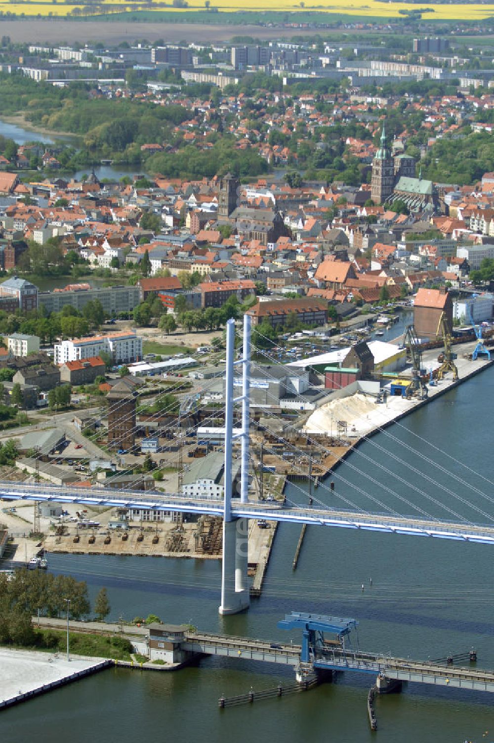 Stralsund from the bird's eye view: Mit dem Begriff Strelasundquerung werden die beiden Brückenverbindungen der Insel Rügen über den Strelasund zum vorpommerschen Festland bei Stralsund, die Rügenbrücke und der Rügendamm, sowie die regelmäßig betriebenen Fährverbindungen zwischen Stralsund und Altefähr sowie Stahlbrode und Glewitz bezeichnet. Der Rügendamm ist die erste feste Strelasundquerung, über den sowohl die alte Bundesstraße 96, als auch eine eingleisige Eisenbahnstrecke sowie ein kombinierter Fuß- und Radweg führen. Sie wurde 1936/1937 fertiggestellt. Rügenbrücke ist der Name der im Jahr 2007 fertiggestellten dreispurigen Hochbrücke ausschließlich für den Kraftfahrzeugverkehr zwischen der Ortschaft Altefähr auf Rügen und der Hanse- und Weltkulturerbestadt Stralsund im Zuge der als Ortsumgehung ausgebauten Bundesstraße 96. Beide Brücken werden parallel betrieben. (DEGES, MAX BÖGL)