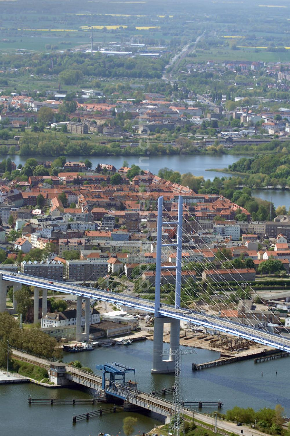 Stralsund from above - Mit dem Begriff Strelasundquerung werden die beiden Brückenverbindungen der Insel Rügen über den Strelasund zum vorpommerschen Festland bei Stralsund, die Rügenbrücke und der Rügendamm, sowie die regelmäßig betriebenen Fährverbindungen zwischen Stralsund und Altefähr sowie Stahlbrode und Glewitz bezeichnet. Der Rügendamm ist die erste feste Strelasundquerung, über den sowohl die alte Bundesstraße 96, als auch eine eingleisige Eisenbahnstrecke sowie ein kombinierter Fuß- und Radweg führen. Sie wurde 1936/1937 fertiggestellt. Rügenbrücke ist der Name der im Jahr 2007 fertiggestellten dreispurigen Hochbrücke ausschließlich für den Kraftfahrzeugverkehr zwischen der Ortschaft Altefähr auf Rügen und der Hanse- und Weltkulturerbestadt Stralsund im Zuge der als Ortsumgehung ausgebauten Bundesstraße 96. Beide Brücken werden parallel betrieben. (DEGES, MAX BÖGL)