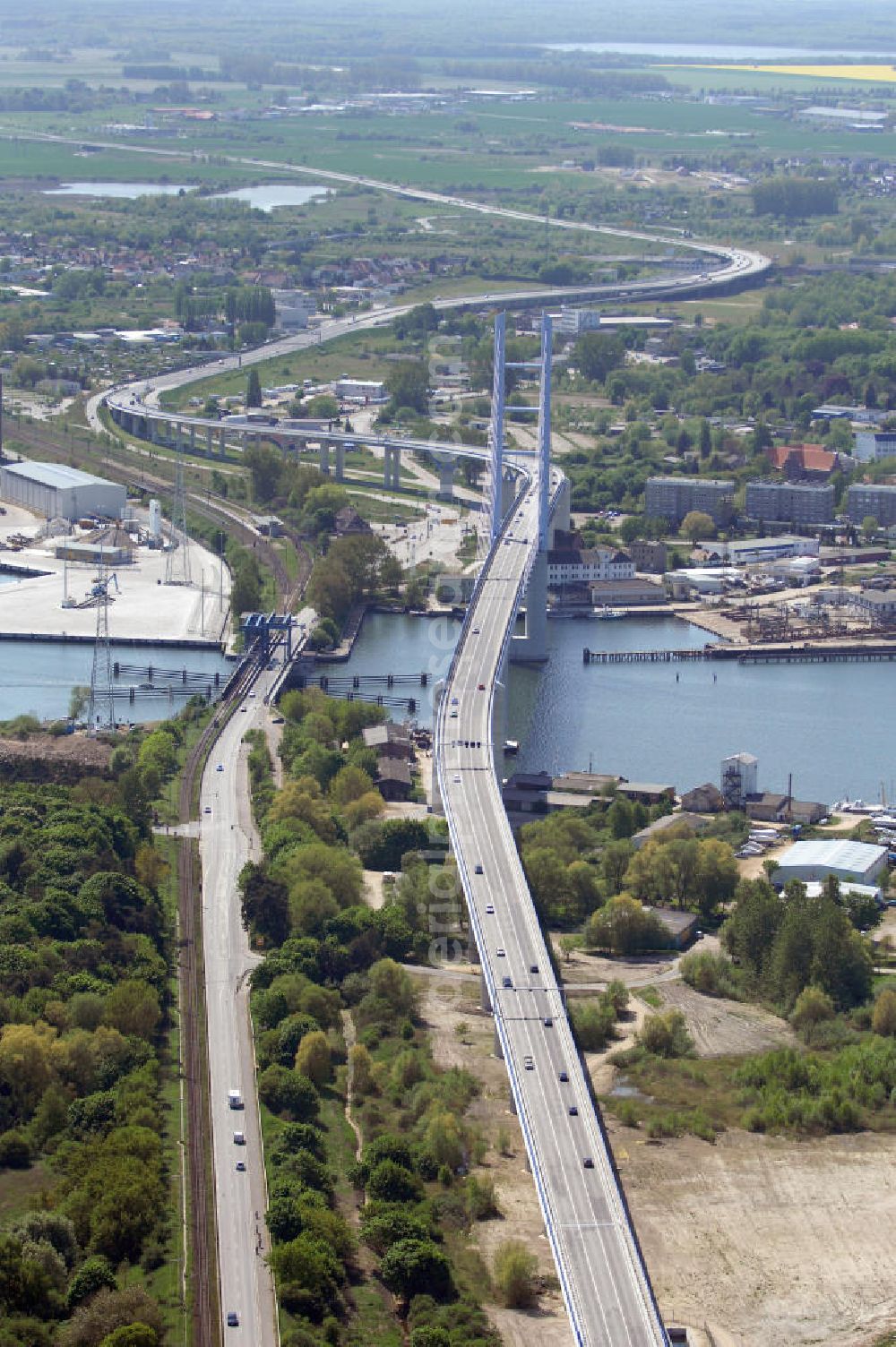 Stralsund from the bird's eye view: Mit dem Begriff Strelasundquerung werden die beiden Brückenverbindungen der Insel Rügen über den Strelasund zum vorpommerschen Festland bei Stralsund, die Rügenbrücke und der Rügendamm, sowie die regelmäßig betriebenen Fährverbindungen zwischen Stralsund und Altefähr sowie Stahlbrode und Glewitz bezeichnet. Der Rügendamm ist die erste feste Strelasundquerung, über den sowohl die alte Bundesstraße 96, als auch eine eingleisige Eisenbahnstrecke sowie ein kombinierter Fuß- und Radweg führen. Sie wurde 1936/1937 fertiggestellt. Rügenbrücke ist der Name der im Jahr 2007 fertiggestellten dreispurigen Hochbrücke ausschließlich für den Kraftfahrzeugverkehr zwischen der Ortschaft Altefähr auf Rügen und der Hanse- und Weltkulturerbestadt Stralsund im Zuge der als Ortsumgehung ausgebauten Bundesstraße 96. Beide Brücken werden parallel betrieben. (DEGES, MAX BÖGL)