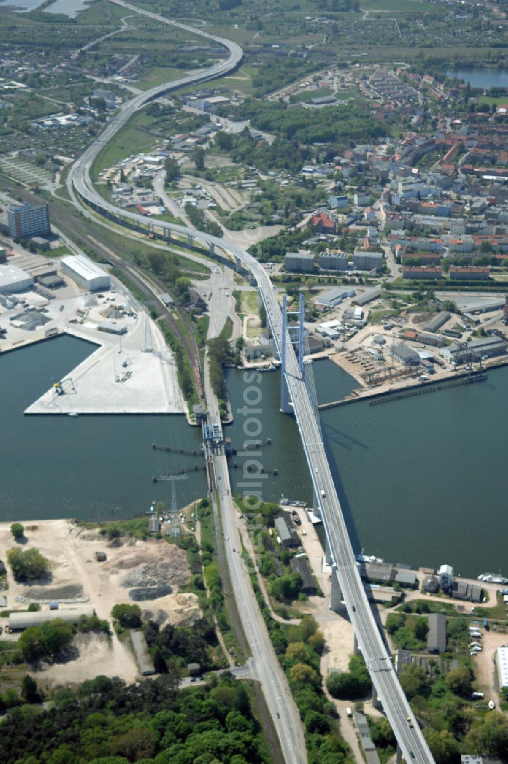 Stralsund from the bird's eye view: Mit dem Begriff Strelasundquerung werden die beiden Brückenverbindungen der Insel Rügen über den Strelasund zum vorpommerschen Festland bei Stralsund, die Rügenbrücke und der Rügendamm, sowie die regelmäßig betriebenen Fährverbindungen zwischen Stralsund und Altefähr sowie Stahlbrode und Glewitz bezeichnet. Der Rügendamm ist die erste feste Strelasundquerung, über den sowohl die alte Bundesstraße 96, als auch eine eingleisige Eisenbahnstrecke sowie ein kombinierter Fuß- und Radweg führen. Sie wurde 1936/1937 fertiggestellt. Rügenbrücke ist der Name der im Jahr 2007 fertiggestellten dreispurigen Hochbrücke ausschließlich für den Kraftfahrzeugverkehr zwischen der Ortschaft Altefähr auf Rügen und der Hanse- und Weltkulturerbestadt Stralsund im Zuge der als Ortsumgehung ausgebauten Bundesstraße 96. Beide Brücken werden parallel betrieben. (DEGES, MAX BÖGL)