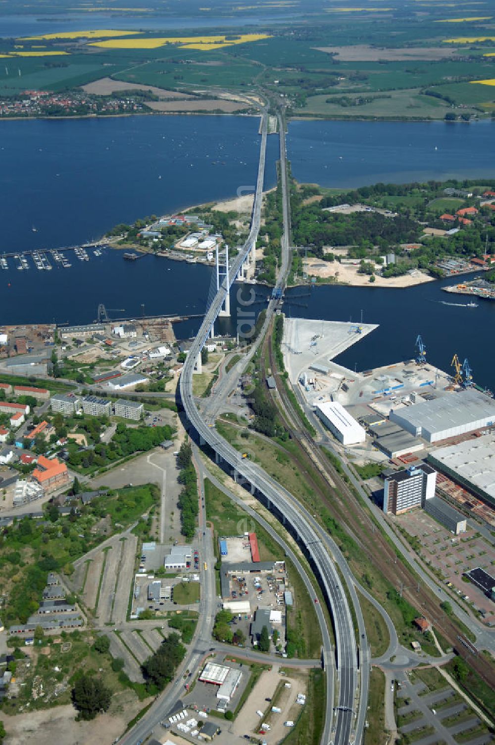 Stralsund from above - Mit dem Begriff Strelasundquerung werden die beiden Brückenverbindungen der Insel Rügen über den Strelasund zum vorpommerschen Festland bei Stralsund, die Rügenbrücke und der Rügendamm, sowie die regelmäßig betriebenen Fährverbindungen zwischen Stralsund und Altefähr sowie Stahlbrode und Glewitz bezeichnet. Der Rügendamm ist die erste feste Strelasundquerung, über den sowohl die alte Bundesstraße 96, als auch eine eingleisige Eisenbahnstrecke sowie ein kombinierter Fuß- und Radweg führen. Sie wurde 1936/1937 fertiggestellt. Rügenbrücke ist der Name der im Jahr 2007 fertiggestellten dreispurigen Hochbrücke ausschließlich für den Kraftfahrzeugverkehr zwischen der Ortschaft Altefähr auf Rügen und der Hanse- und Weltkulturerbestadt Stralsund im Zuge der als Ortsumgehung ausgebauten Bundesstraße 96. Beide Brücken werden parallel betrieben. (DEGES, MAX BÖGL)