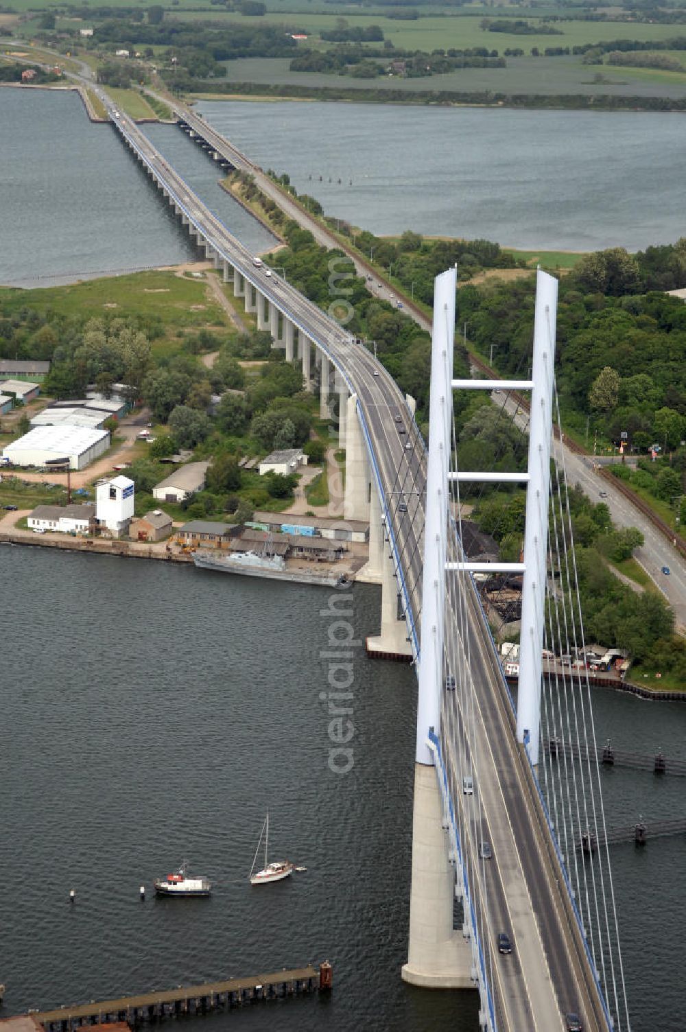 Stralsund from the bird's eye view: Mit dem Begriff Strelasundquerung werden die beiden Brückenverbindungen der Insel Rügen über den Strelasund zum vorpommerschen Festland bei Stralsund, die Rügenbrücke und der Rügendamm , sowie die regelmäßig betriebenen Fährverbindungen zwischen Stralsund und Altefähr sowie Stahlbrode und Glewitz bezeichnet. Der Rügendamm ist die erste feste Strelasundquerung, über den sowohl die alte Bundesstraße 96, als auch eine eingleisige Eisenbahnstrecke sowie ein kombinierter Fuß- und Radweg führen. Sie wurde 1936/1937 fertiggestellt. Rügenbrücke ist der Name der im Jahr 2007 fertiggestellten dreispurigen Hochbrücke ausschließlich für den Kraftfahrzeugverkehr zwischen der Ortschaft Altefähr auf Rügen und der Hanse- und Weltkulturerbestadt Stralsund im Zuge der als Ortsumgehung ausgebauten Bundesstraße 96. Beide Brücken werden parallel betrieben. (DEGES, MAX BÖGL)