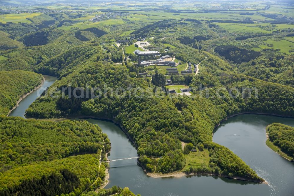 Schleiden from the bird's eye view: Dam and shore areas at the lake Urfttalsperre near Schleiden in the state North Rhine-Westphalia. In view of the complex of buildings of the former Nazi Ordensburg Vogelsang, later barracks of the Belgian armed forces and today's Meeting Centre International Place in the Eifel National Park