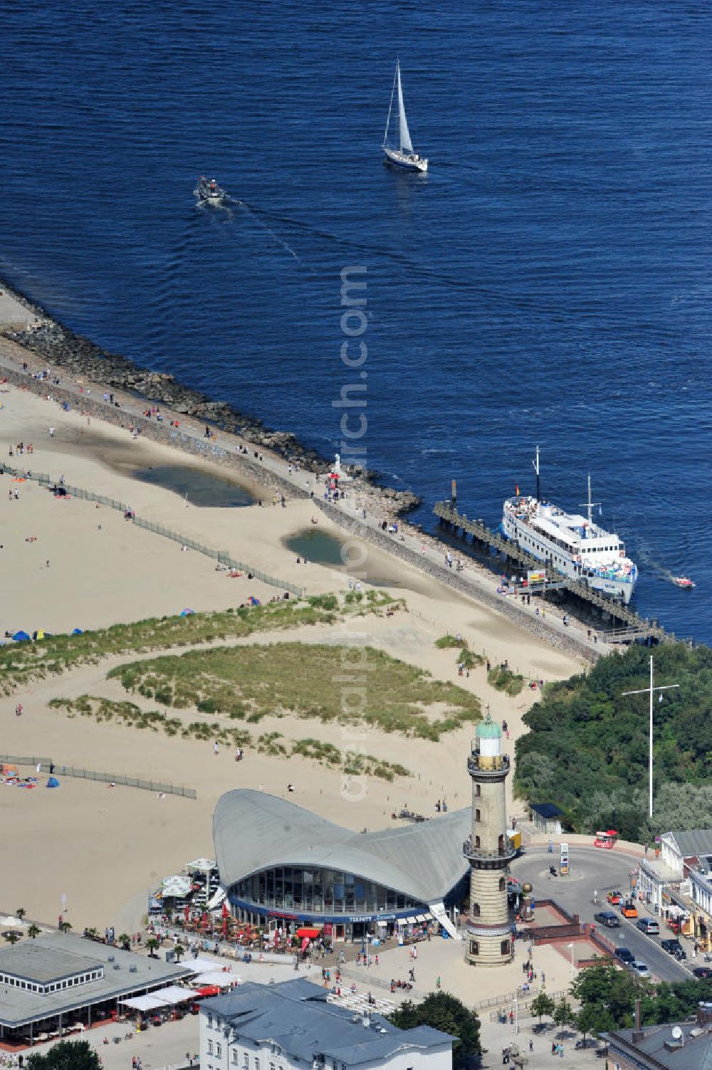 Rostock - Warnemünde from the bird's eye view: Blick auf die den Teepott mit dem alten Leuchtturman der Seepromenade des Ostseestrandes von Warnemünde. Der 1967 errichtete Teepott neben dem Leuchtturm an der Warnemünder Seepromenade erbaute Einzelbau ist ein Beispiel für die Hyparschalenarchitektur der 1960er Jahre. Er beherbergt unter an derem zwei Restaurants und eine ständige Ausstellung des Weltenbummlers Reinhold Kasten. Views of the lake with the Teepott and the old lighthouse at the Baltic Sea beach of Warnemünde.