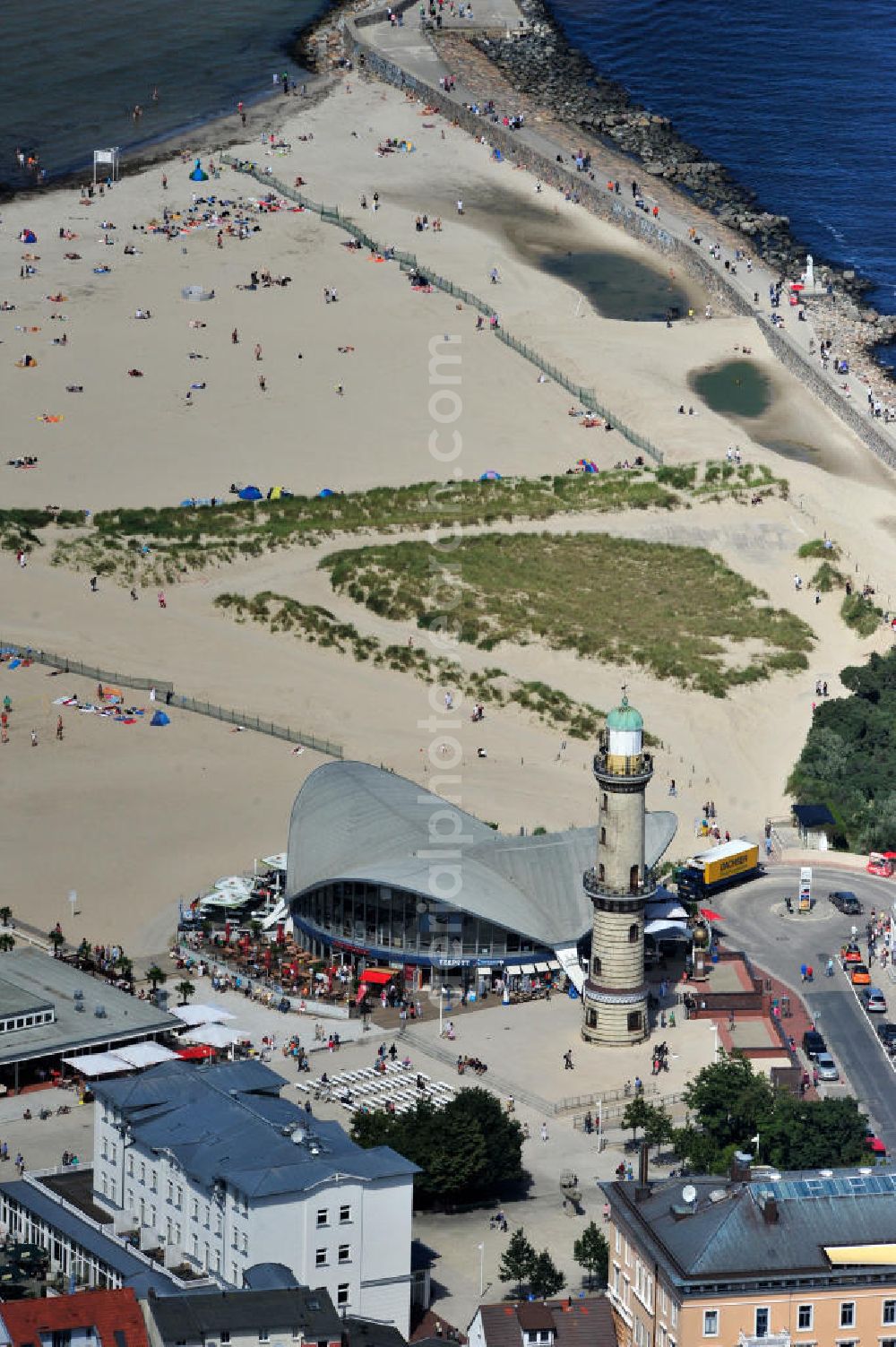 Aerial image Rostock - Warnemünde - Blick auf die den Teepott mit dem alten Leuchtturman der Seepromenade des Ostseestrandes von Warnemünde. Der 1967 errichtete Teepott neben dem Leuchtturm an der Warnemünder Seepromenade erbaute Einzelbau ist ein Beispiel für die Hyparschalenarchitektur der 1960er Jahre. Er beherbergt unter an derem zwei Restaurants und eine ständige Ausstellung des Weltenbummlers Reinhold Kasten. Views of the lake with the Teepott and the old lighthouse at the Baltic Sea beach of Warnemünde.