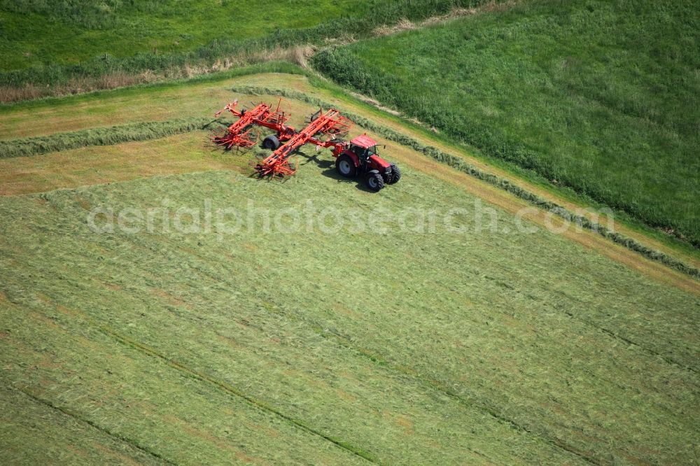 Rieseby from above - Tractor and agricultural field work in the Hoerst part of Rieseby in the state of Schleswig-Holstein. The island Schwansen is mostly used agriculturally. The red vehicle moves symmetrically through the field during harvest