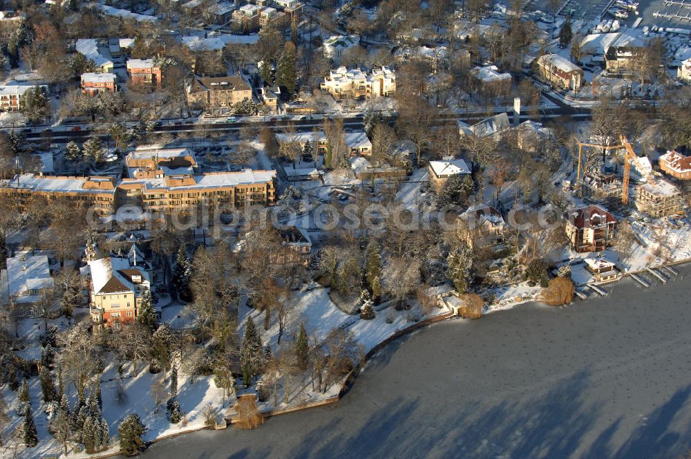 Aerial photograph Berlin - Blick auf den winterlich mit Schnee bedeckten Uferbereich an der Villa Siemens Am Kleinen Wannsee direkt gegenüber des Neubaus zum Immanuel-Krankenhauses in Berlin-Wannsee. Das Krankenhaus gehört zur Immanuel Diakonie Group (IDG), die eine Einrichtung der Evangelisch-Freikirchlichen Gemeinde Berlin-Schöneberg ist. Die Verwaltung der IDG hatte ihren Sitz in der Villa Siemens. Das Gebäude war einst eine Sommerresidenz von Arnold von Siemens, dem ältesten Sohn des Firmengründers Werner von Siemens. Die Architekten waren Paul und Walther Hentschel, 1888 wurde der Bau fertiggestellt. Die Villa Siemens gehörte zur Colonie Alsen, einer Siedlung für das Berliner Großbürgertum, die Wilhelm Conrad 1863 gegründet hatte. Nach dem Zweiten Weltkrieg stifteten Hermann und Charlotte von Siemens die Villa der Baptisten-Gemeinde mit der Auflage, sie für soziale Zwecke zu nutzen. Es ist das einzige Ensemble von Gebäude und Park der ehemaligen Kolonie, das bis heute erhalten geblieben ist. Der Krankenhausbetrieb ist jetzt in einem Neubau auf der gegenüberliegenden Straßenseite untergebracht. Das ehemals zum Areal gehörende Anwesen Am kleinen Wannsee Nr 4 wurde verkauft. ISA IMMOBILEN AGENTUR GmbH, Herr Roland Kober