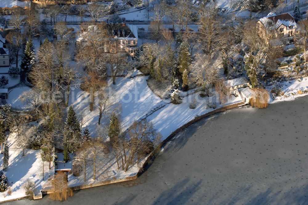 Berlin from above - Blick auf den winterlich mit Schnee bedeckten Uferbereich an der Villa Siemens Am Kleinen Wannsee direkt gegenüber des Neubaus zum Immanuel-Krankenhauses in Berlin-Wannsee. Das Krankenhaus gehört zur Immanuel Diakonie Group (IDG), die eine Einrichtung der Evangelisch-Freikirchlichen Gemeinde Berlin-Schöneberg ist. Die Verwaltung der IDG hatte ihren Sitz in der Villa Siemens. Das Gebäude war einst eine Sommerresidenz von Arnold von Siemens, dem ältesten Sohn des Firmengründers Werner von Siemens. Die Architekten waren Paul und Walther Hentschel, 1888 wurde der Bau fertiggestellt. Die Villa Siemens gehörte zur Colonie Alsen, einer Siedlung für das Berliner Großbürgertum, die Wilhelm Conrad 1863 gegründet hatte. Nach dem Zweiten Weltkrieg stifteten Hermann und Charlotte von Siemens die Villa der Baptisten-Gemeinde mit der Auflage, sie für soziale Zwecke zu nutzen. Es ist das einzige Ensemble von Gebäude und Park der ehemaligen Kolonie, das bis heute erhalten geblieben ist. Der Krankenhausbetrieb ist jetzt in einem Neubau auf der gegenüberliegenden Straßenseite untergebracht. Das ehemals zum Areal gehörende Anwesen Am kleinen Wannsee Nr 4 wurde verkauft. ISA IMMOBILEN AGENTUR GmbH, Herr Roland Kober