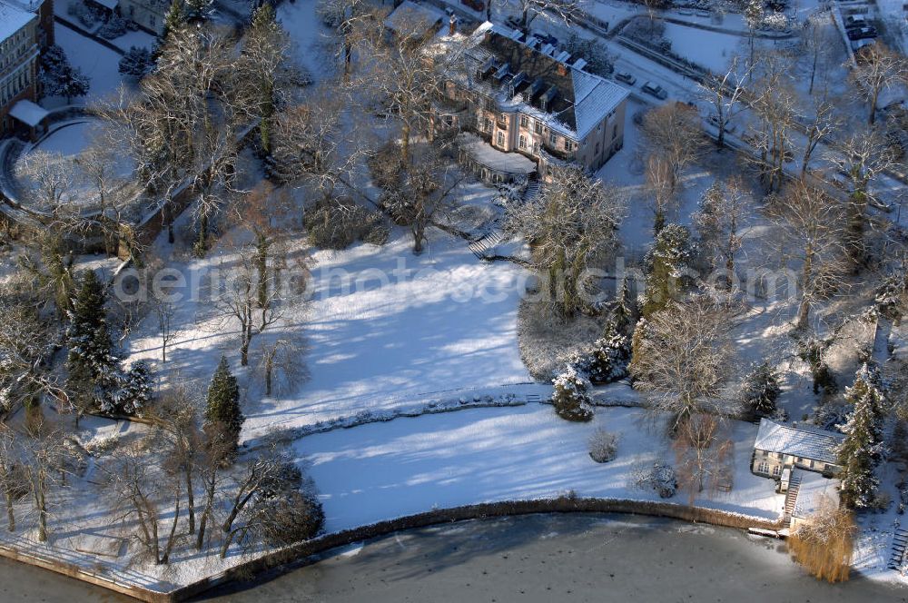 Aerial image Berlin - Blick auf den winterlich mit Schnee bedeckten Uferbereich an der Villa Siemens Am Kleinen Wannsee direkt gegenüber des Neubaus zum Immanuel-Krankenhauses in Berlin-Wannsee. Das Krankenhaus gehört zur Immanuel Diakonie Group (IDG), die eine Einrichtung der Evangelisch-Freikirchlichen Gemeinde Berlin-Schöneberg ist. Die Verwaltung der IDG hatte ihren Sitz in der Villa Siemens. Das Gebäude war einst eine Sommerresidenz von Arnold von Siemens, dem ältesten Sohn des Firmengründers Werner von Siemens. Die Architekten waren Paul und Walther Hentschel, 1888 wurde der Bau fertiggestellt. Die Villa Siemens gehörte zur Colonie Alsen, einer Siedlung für das Berliner Großbürgertum, die Wilhelm Conrad 1863 gegründet hatte. Nach dem Zweiten Weltkrieg stifteten Hermann und Charlotte von Siemens die Villa der Baptisten-Gemeinde mit der Auflage, sie für soziale Zwecke zu nutzen. Es ist das einzige Ensemble von Gebäude und Park der ehemaligen Kolonie, das bis heute erhalten geblieben ist. Der Krankenhausbetrieb ist jetzt in einem Neubau auf der gegenüberliegenden Straßenseite untergebracht. Das ehemals zum Areal gehörende Anwesen Am kleinen Wannsee Nr 4 wurde verkauft. ISA IMMOBILEN AGENTUR GmbH, Herr Roland Kober