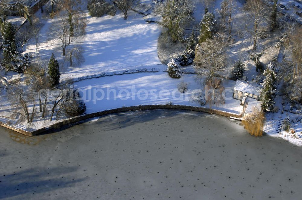 Aerial photograph Berlin - Blick auf den winterlich mit Schnee bedeckten Uferbereich an der Villa Siemens Am Kleinen Wannsee direkt gegenüber des Neubaus zum Immanuel-Krankenhauses in Berlin-Wannsee. Das Krankenhaus gehört zur Immanuel Diakonie Group (IDG), die eine Einrichtung der Evangelisch-Freikirchlichen Gemeinde Berlin-Schöneberg ist. Die Verwaltung der IDG hatte ihren Sitz in der Villa Siemens. Das Gebäude war einst eine Sommerresidenz von Arnold von Siemens, dem ältesten Sohn des Firmengründers Werner von Siemens. Die Architekten waren Paul und Walther Hentschel, 1888 wurde der Bau fertiggestellt. Die Villa Siemens gehörte zur Colonie Alsen, einer Siedlung für das Berliner Großbürgertum, die Wilhelm Conrad 1863 gegründet hatte. Nach dem Zweiten Weltkrieg stifteten Hermann und Charlotte von Siemens die Villa der Baptisten-Gemeinde mit der Auflage, sie für soziale Zwecke zu nutzen. Es ist das einzige Ensemble von Gebäude und Park der ehemaligen Kolonie, das bis heute erhalten geblieben ist. Der Krankenhausbetrieb ist jetzt in einem Neubau auf der gegenüberliegenden Straßenseite untergebracht. Das ehemals zum Areal gehörende Anwesen Am kleinen Wannsee Nr 4 wurde verkauft. ISA IMMOBILEN AGENTUR GmbH, Herr Roland Kober