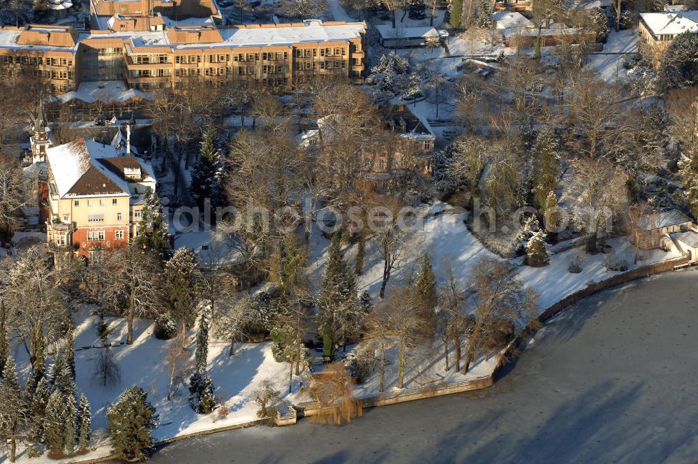 Berlin from the bird's eye view: Blick auf den winterlich mit Schnee bedeckten Uferbereich an der Villa Siemens Am Kleinen Wannsee direkt gegenüber des Neubaus zum Immanuel-Krankenhauses in Berlin-Wannsee. Das Krankenhaus gehört zur Immanuel Diakonie Group (IDG), die eine Einrichtung der Evangelisch-Freikirchlichen Gemeinde Berlin-Schöneberg ist. Die Verwaltung der IDG hatte ihren Sitz in der Villa Siemens. Das Gebäude war einst eine Sommerresidenz von Arnold von Siemens, dem ältesten Sohn des Firmengründers Werner von Siemens. Die Architekten waren Paul und Walther Hentschel, 1888 wurde der Bau fertiggestellt. Die Villa Siemens gehörte zur Colonie Alsen, einer Siedlung für das Berliner Großbürgertum, die Wilhelm Conrad 1863 gegründet hatte. Nach dem Zweiten Weltkrieg stifteten Hermann und Charlotte von Siemens die Villa der Baptisten-Gemeinde mit der Auflage, sie für soziale Zwecke zu nutzen. Es ist das einzige Ensemble von Gebäude und Park der ehemaligen Kolonie, das bis heute erhalten geblieben ist. Der Krankenhausbetrieb ist jetzt in einem Neubau auf der gegenüberliegenden Straßenseite untergebracht. Das ehemals zum Areal gehörende Anwesen Am kleinen Wannsee Nr 4 wurde verkauft. ISA IMMOBILEN AGENTUR GmbH, Herr Roland Kober