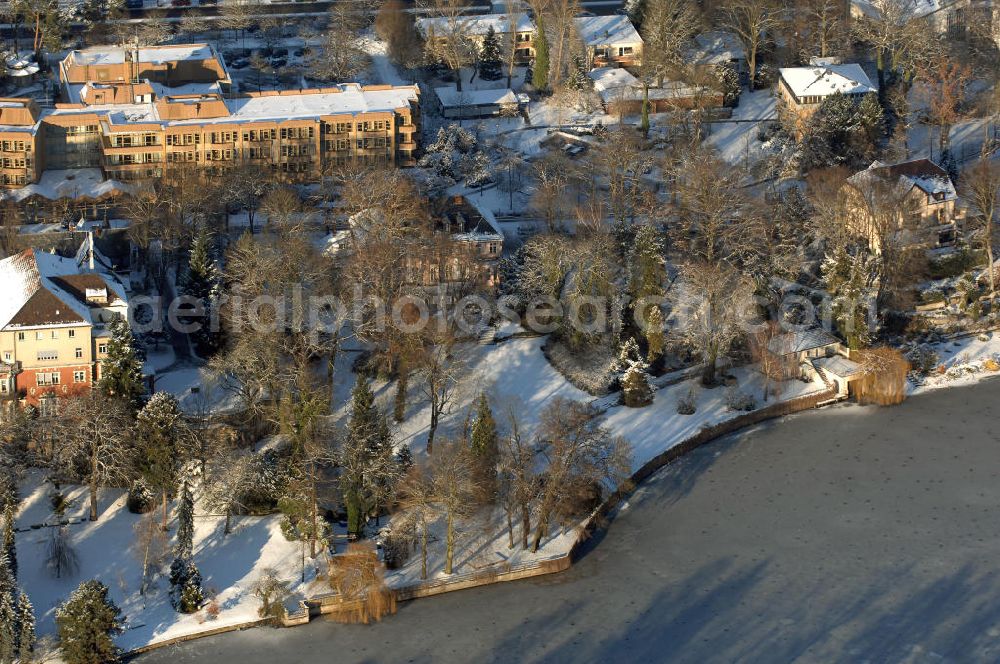 Aerial image Berlin - Blick auf den winterlich mit Schnee bedeckten Uferbereich an der Villa Siemens Am Kleinen Wannsee direkt gegenüber des Neubaus zum Immanuel-Krankenhauses in Berlin-Wannsee. Das Krankenhaus gehört zur Immanuel Diakonie Group (IDG), die eine Einrichtung der Evangelisch-Freikirchlichen Gemeinde Berlin-Schöneberg ist. Die Verwaltung der IDG hatte ihren Sitz in der Villa Siemens. Das Gebäude war einst eine Sommerresidenz von Arnold von Siemens, dem ältesten Sohn des Firmengründers Werner von Siemens. Die Architekten waren Paul und Walther Hentschel, 1888 wurde der Bau fertiggestellt. Die Villa Siemens gehörte zur Colonie Alsen, einer Siedlung für das Berliner Großbürgertum, die Wilhelm Conrad 1863 gegründet hatte. Nach dem Zweiten Weltkrieg stifteten Hermann und Charlotte von Siemens die Villa der Baptisten-Gemeinde mit der Auflage, sie für soziale Zwecke zu nutzen. Es ist das einzige Ensemble von Gebäude und Park der ehemaligen Kolonie, das bis heute erhalten geblieben ist. Der Krankenhausbetrieb ist jetzt in einem Neubau auf der gegenüberliegenden Straßenseite untergebracht. Das ehemals zum Areal gehörende Anwesen Am kleinen Wannsee Nr 4 wurde verkauft. ISA IMMOBILEN AGENTUR GmbH, Herr Roland Kober