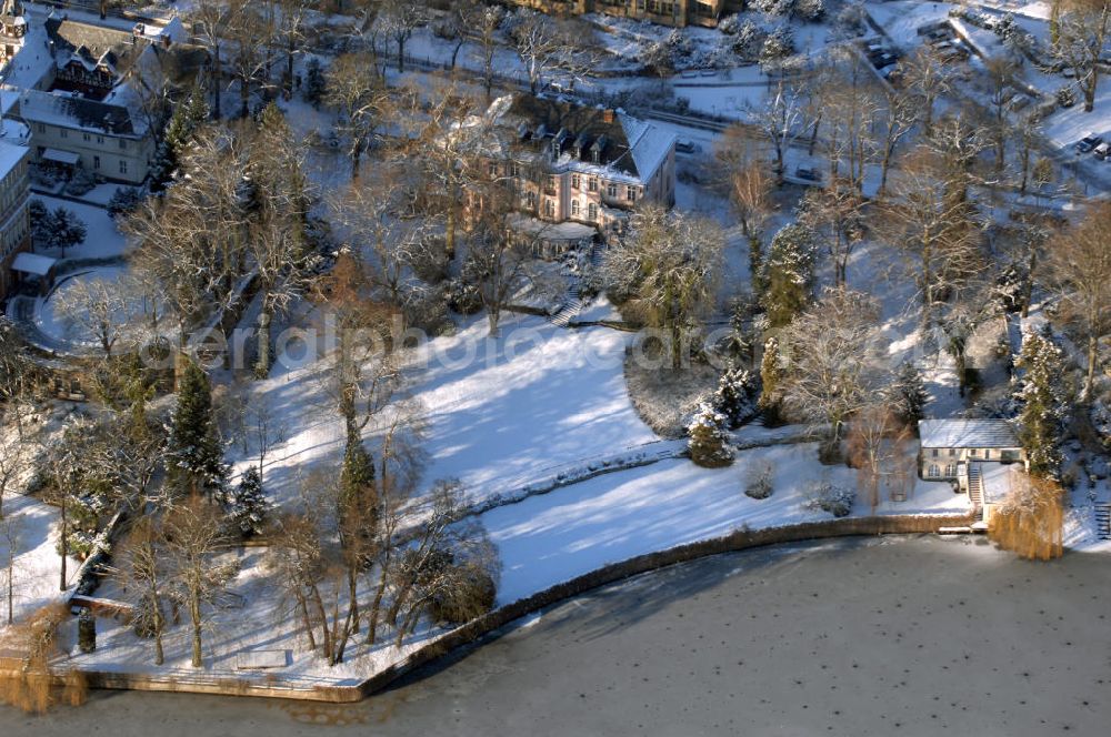 Aerial photograph Berlin - Blick auf den winterlich mit Schnee bedeckten Uferbereich an der Villa Siemens Am Kleinen Wannsee direkt gegenüber des Neubaus zum Immanuel-Krankenhauses in Berlin-Wannsee. Das Krankenhaus gehört zur Immanuel Diakonie Group (IDG), die eine Einrichtung der Evangelisch-Freikirchlichen Gemeinde Berlin-Schöneberg ist. Die Verwaltung der IDG hatte ihren Sitz in der Villa Siemens. Das Gebäude war einst eine Sommerresidenz von Arnold von Siemens, dem ältesten Sohn des Firmengründers Werner von Siemens. Die Architekten waren Paul und Walther Hentschel, 1888 wurde der Bau fertiggestellt. Die Villa Siemens gehörte zur Colonie Alsen, einer Siedlung für das Berliner Großbürgertum, die Wilhelm Conrad 1863 gegründet hatte. Nach dem Zweiten Weltkrieg stifteten Hermann und Charlotte von Siemens die Villa der Baptisten-Gemeinde mit der Auflage, sie für soziale Zwecke zu nutzen. Es ist das einzige Ensemble von Gebäude und Park der ehemaligen Kolonie, das bis heute erhalten geblieben ist. Der Krankenhausbetrieb ist jetzt in einem Neubau auf der gegenüberliegenden Straßenseite untergebracht. Das ehemals zum Areal gehörende Anwesen Am kleinen Wannsee Nr 4 wurde verkauft. ISA IMMOBILEN AGENTUR GmbH, Herr Roland Kober