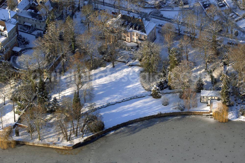 Berlin from the bird's eye view: Blick auf den winterlich mit Schnee bedeckten Uferbereich an der Villa Siemens Am Kleinen Wannsee direkt gegenüber des Neubaus zum Immanuel-Krankenhauses in Berlin-Wannsee. Das Krankenhaus gehört zur Immanuel Diakonie Group (IDG), die eine Einrichtung der Evangelisch-Freikirchlichen Gemeinde Berlin-Schöneberg ist. Die Verwaltung der IDG hatte ihren Sitz in der Villa Siemens. Das Gebäude war einst eine Sommerresidenz von Arnold von Siemens, dem ältesten Sohn des Firmengründers Werner von Siemens. Die Architekten waren Paul und Walther Hentschel, 1888 wurde der Bau fertiggestellt. Die Villa Siemens gehörte zur Colonie Alsen, einer Siedlung für das Berliner Großbürgertum, die Wilhelm Conrad 1863 gegründet hatte. Nach dem Zweiten Weltkrieg stifteten Hermann und Charlotte von Siemens die Villa der Baptisten-Gemeinde mit der Auflage, sie für soziale Zwecke zu nutzen. Es ist das einzige Ensemble von Gebäude und Park der ehemaligen Kolonie, das bis heute erhalten geblieben ist. Der Krankenhausbetrieb ist jetzt in einem Neubau auf der gegenüberliegenden Straßenseite untergebracht. Das ehemals zum Areal gehörende Anwesen Am kleinen Wannsee Nr 4 wurde verkauft. ISA IMMOBILEN AGENTUR GmbH, Herr Roland Kober