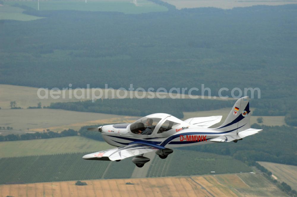 Aerial image Reckenthin - Ein modernes Ganzmetall-Ultraleichtflugzeug Eurostar über dem brandenburgischen Reckenthin. Es ist ein 2-Sitziges Ultraleichtflugzeug, das von der Firma Evektor-Aerotechnik aus Kunovice in Tschechien hergestellt wird und ab 1997 in den deutschen Markt eingeführt wurde. Nach Deutschland wird das Flugzeug vom Flugsportzentrum in Bautzen importiert.Das Flugzeug ist eine moderne Tiefdeckerkonstruktion aus Aluminium. Es hat eine Gleitzahl 1:10 und wird ständig verbessert. Letzte größere Änderungen erfolgten 2004 mit der Zulassung einer Variante mit der Bezeichnung Modell 2000/R für eine Startmasse von 472,5 kg Angetrieben wird der Eurostar von einem Rotax-Motor mit 80 bzw 100 PS. Von seinen Flugleistungen und seinem Platzangebot ist er vergleichbar mit kleinen 2-sitzigen Flugzeugen.