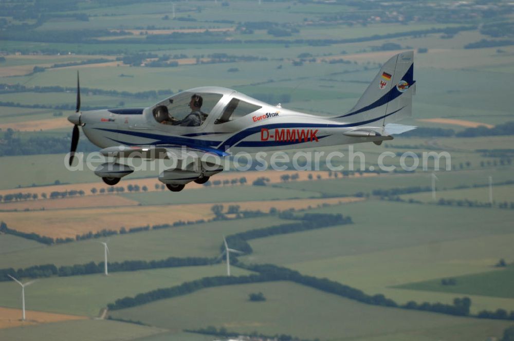 Reckenthin from the bird's eye view: Ein modernes Ganzmetall-Ultraleichtflugzeug Eurostar über dem brandenburgischen Reckenthin. Es ist ein 2-Sitziges Ultraleichtflugzeug, das von der Firma Evektor-Aerotechnik aus Kunovice in Tschechien hergestellt wird und ab 1997 in den deutschen Markt eingeführt wurde. Nach Deutschland wird das Flugzeug vom Flugsportzentrum in Bautzen importiert.Das Flugzeug ist eine moderne Tiefdeckerkonstruktion aus Aluminium. Es hat eine Gleitzahl 1:10 und wird ständig verbessert. Letzte größere Änderungen erfolgten 2004 mit der Zulassung einer Variante mit der Bezeichnung Modell 2000/R für eine Startmasse von 472,5 kg Angetrieben wird der Eurostar von einem Rotax-Motor mit 80 bzw 100 PS. Von seinen Flugleistungen und seinem Platzangebot ist er vergleichbar mit kleinen 2-sitzigen Flugzeugen.