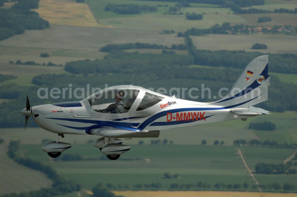 Aerial image Reckenthin - Ein modernes Ganzmetall-Ultraleichtflugzeug Eurostar über dem brandenburgischen Reckenthin. Es ist ein 2-Sitziges Ultraleichtflugzeug, das von der Firma Evektor-Aerotechnik aus Kunovice in Tschechien hergestellt wird und ab 1997 in den deutschen Markt eingeführt wurde. Nach Deutschland wird das Flugzeug vom Flugsportzentrum in Bautzen importiert.Das Flugzeug ist eine moderne Tiefdeckerkonstruktion aus Aluminium. Es hat eine Gleitzahl 1:10 und wird ständig verbessert. Letzte größere Änderungen erfolgten 2004 mit der Zulassung einer Variante mit der Bezeichnung Modell 2000/R für eine Startmasse von 472,5 kg Angetrieben wird der Eurostar von einem Rotax-Motor mit 80 bzw 100 PS. Von seinen Flugleistungen und seinem Platzangebot ist er vergleichbar mit kleinen 2-sitzigen Flugzeugen.