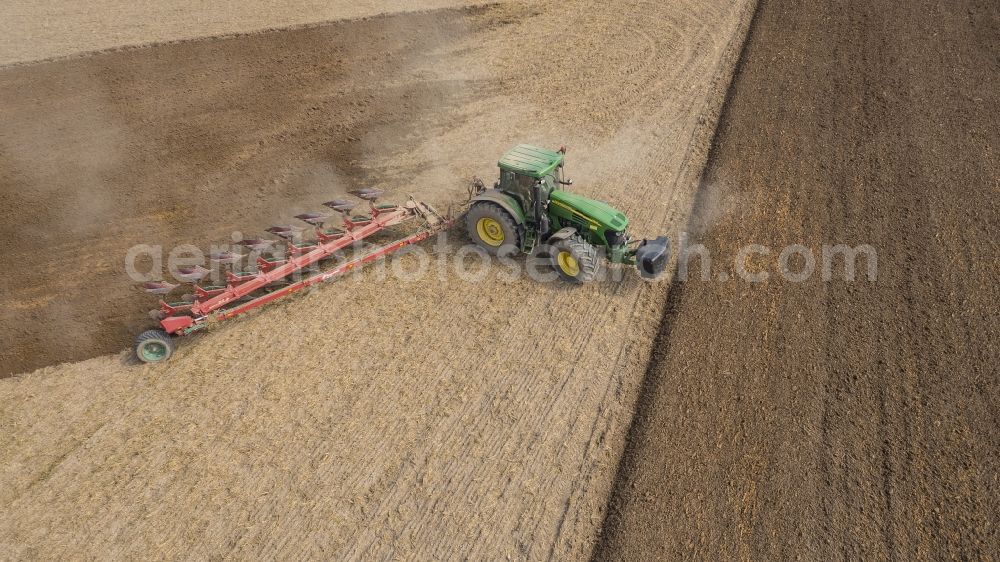 Sauheim from the bird's eye view: Plowing and shifting the earth by a tractor with plow on agricultural fields in Sauheim in the state Bavaria