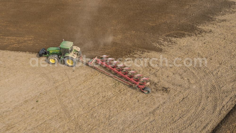 Aerial photograph Sauheim - Plowing and shifting the earth by a tractor with plow on agricultural fields in Sauheim in the state Bavaria