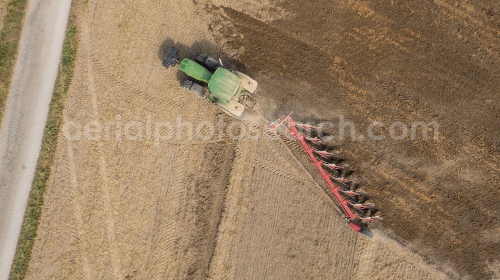 Sauheim from the bird's eye view: Plowing and shifting the earth by a tractor with plow on agricultural fields in Sauheim in the state Bavaria