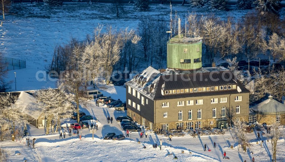 Winterberg from above - Winterly hotel-restaurant and Asten Tower on the snow-covered mountain Kahler Asten in Winterberg in the state of North Rhine-Westphalia. The mountain is the third highest in the Rothaar Mountain Range region. On top of the mountain sits the hotel-restaurant and the green tower. It is also part of the winter sports resort of Skiliftkarussell Winterberg